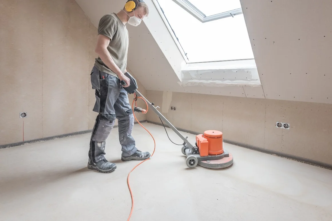 Person schleift Estrich mit Schleifmaschine